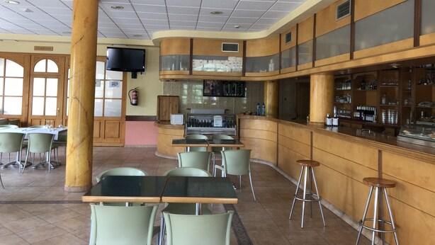 A restaurant with a bar area, multiple tables and chairs, and a television mounted on the wall. - Hotel Silos 2000 (Santo Domingo de Silos)