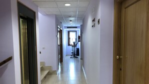 A hallway with a wooden door on the right, a staircase on the left, and a fitness machine in the center. - Hotel Silos 2000 (Santo Domingo de Silos)