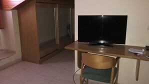 A room with a wooden desk, a television, a chair, and a sliding glass door leading to a shower area. - Hotel Silos 2000 (Santo Domingo de Silos)