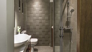 A modern bathroom with a glass-enclosed shower, a white sink, and a toilet. - Olvios Design Suite (Thessaloniki)
