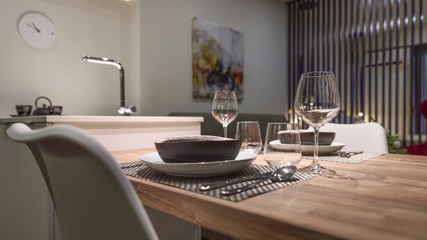 A dining table set with plates, glasses, and cutlery, a clock, and a modern abstract painting on the wall. - Olvios Design Suite (Thessaloniki)