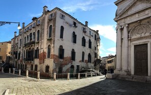 A historic building with arched windows and a stone facade, adjacent to a classical building with a large door and columns. - Suites alla Maddalena (Venice)