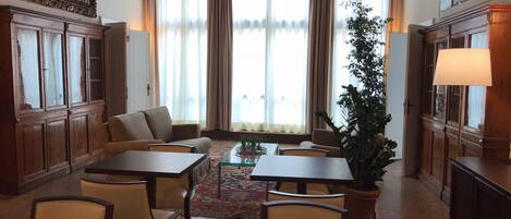 A traditional room with a sofa, two tables, chairs, a potted plant, and a lamp.