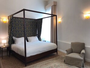 A four-poster bed with a canopy, a bedside table with a lamp, a chair, and a patterned carpet. - Suites alla Maddalena (Venice)