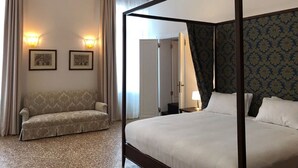 A four-poster bed with a dark frame, a sofa with a patterned upholstery, and two wall-mounted lights. - Suites alla Maddalena (Venice)