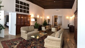 A spacious living area with a high ceiling, a large wooden cabinet, a sofa, a coffee table, and a patterned rug. - Suites alla Maddalena (Venice)