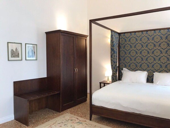 A bedroom with a four-poster bed, a wooden wardrobe, and a nightstand with a lamp. - Suites alla Maddalena (Venice)