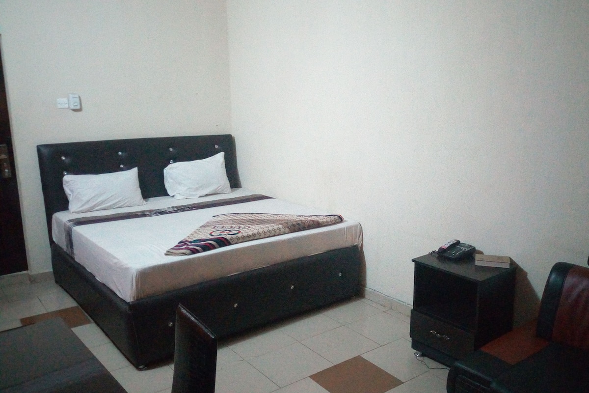 A small, simple room with a bed, a nightstand, a chair, and a small table.