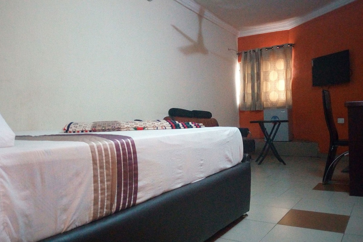 A hotel room with a bed, a small table, a chair, and a TV mounted on the wall.