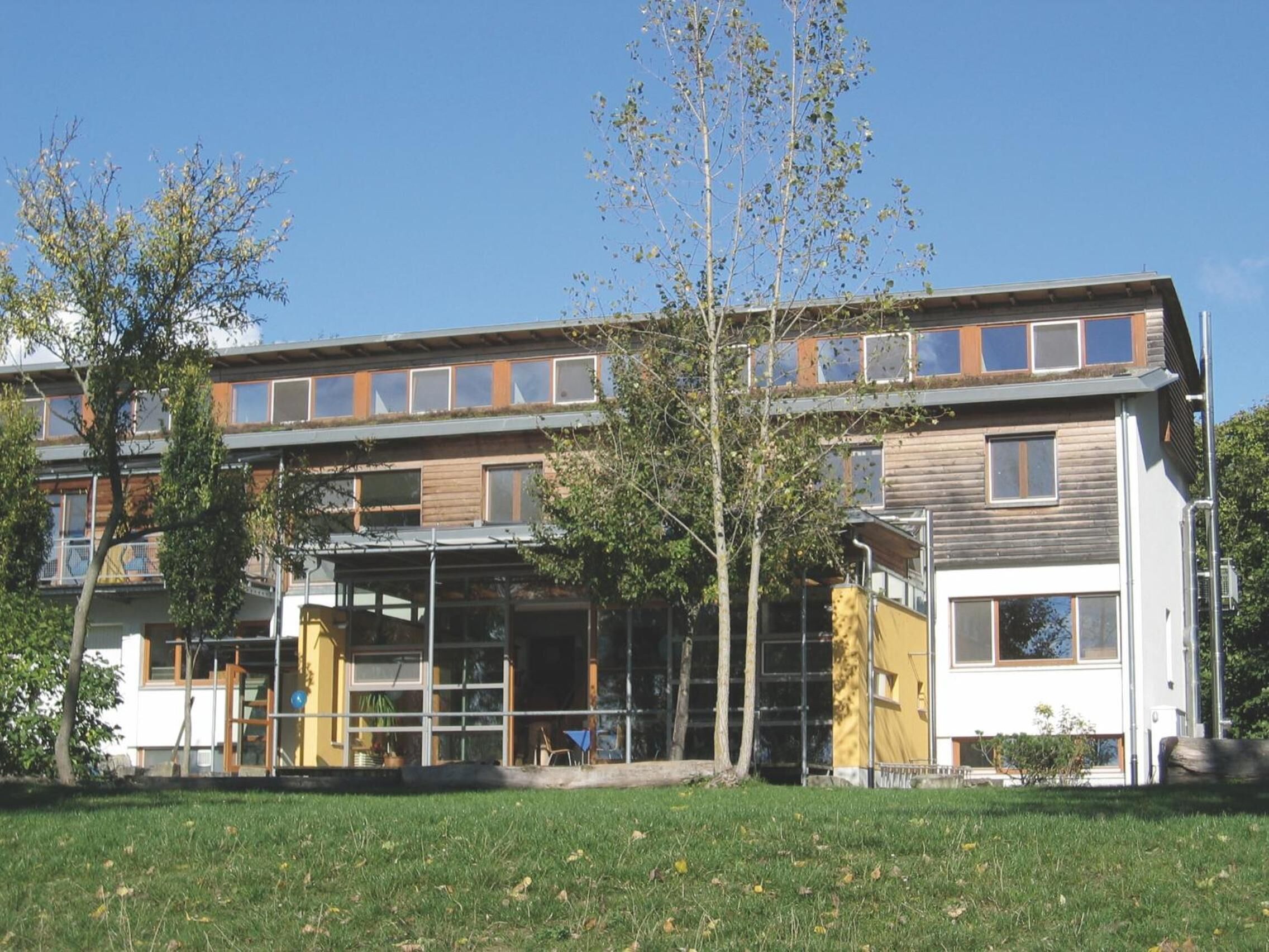 A modern multi-story building with a flat roof, large windows, and a covered entrance area.