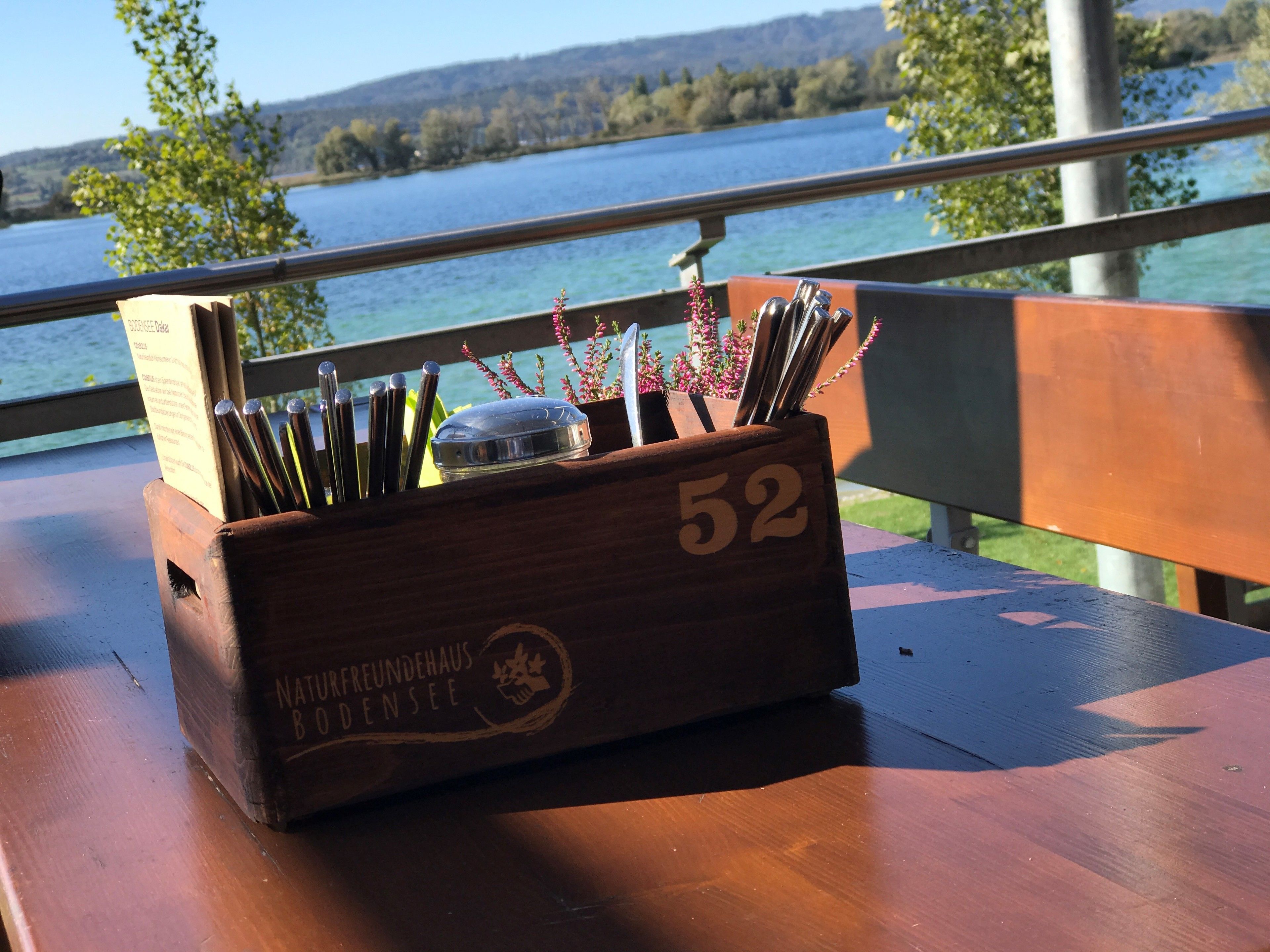 A wooden box with the number 52 on it, placed on a wooden table with a view of a lake and trees in the background.