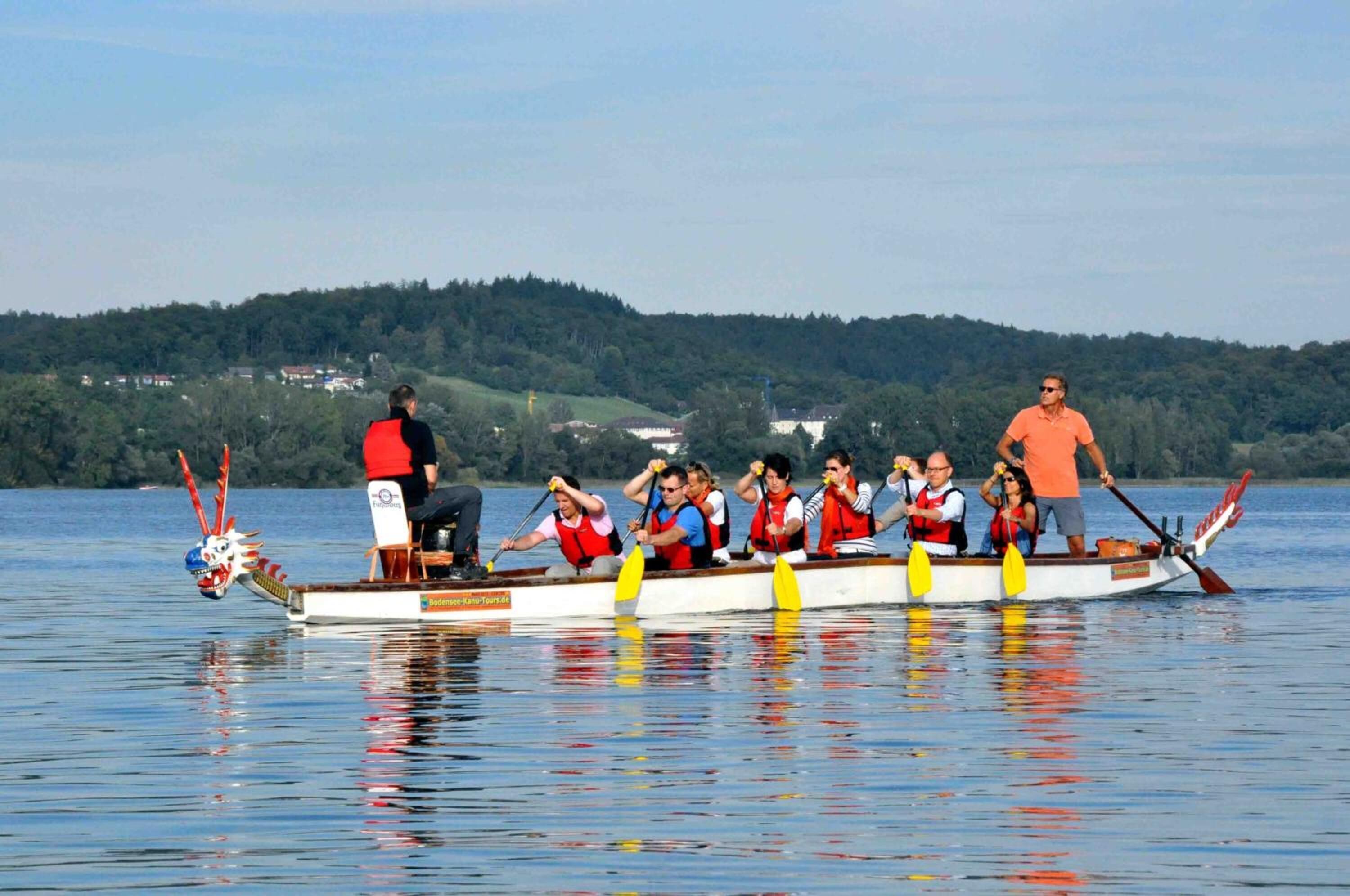 Ein Drachenboot mit mehreren Ruderern, ein Steuermann vorne und eine Frau hinten.