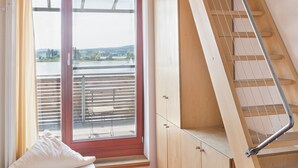 Een kamer met een houten trap, een raam met uitzicht, een ronde tafel en een stoel.