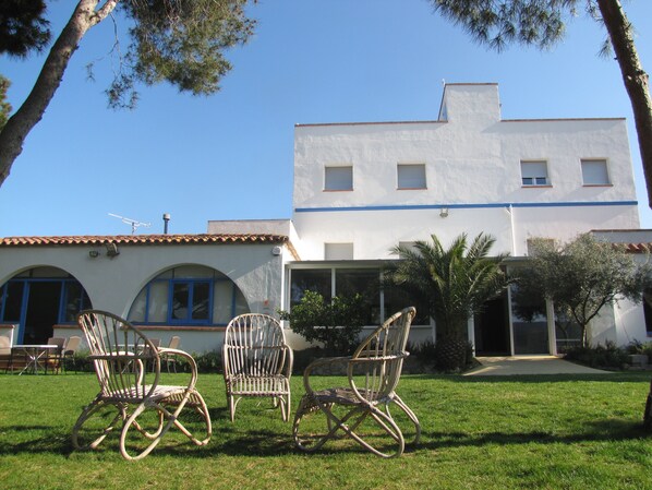 A two-story building with a white exterior and blue trim, featuring a patio with wicker chairs and a small table.