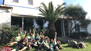 A group of people sitting on grass in front of a building with a palm tree. - Alberg Costa Brava - Hostel (Llanca)
