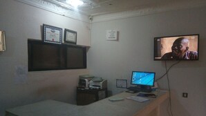A hotel reception desk with a computer monitor, a telephone, and a television mounted on the wall. - Progandy Guest House Annex (Abuja)