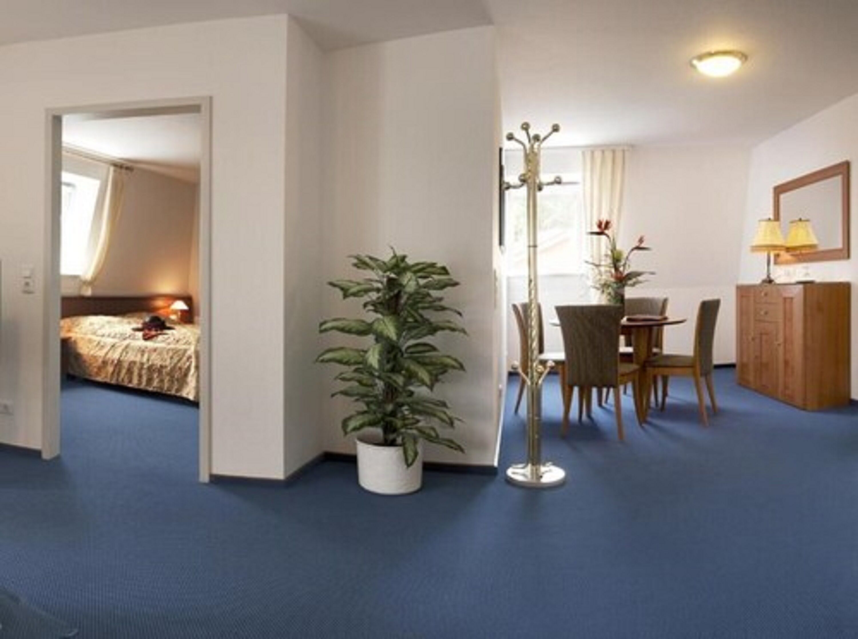 Een hotelkamer met een bed, een eettafel met stoelen, een plant in pot en een kapstok.