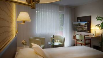 Hotelkamer met een groot bed, twee fauteuils, een klein rond tafeltje met een fles en glazen, een bureau met een stoel, een aan de muur bevestigde televisie en een plant.