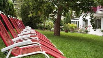 A row of red and white lounge chairs aligned along a grassy area with a tree and a building in the background.