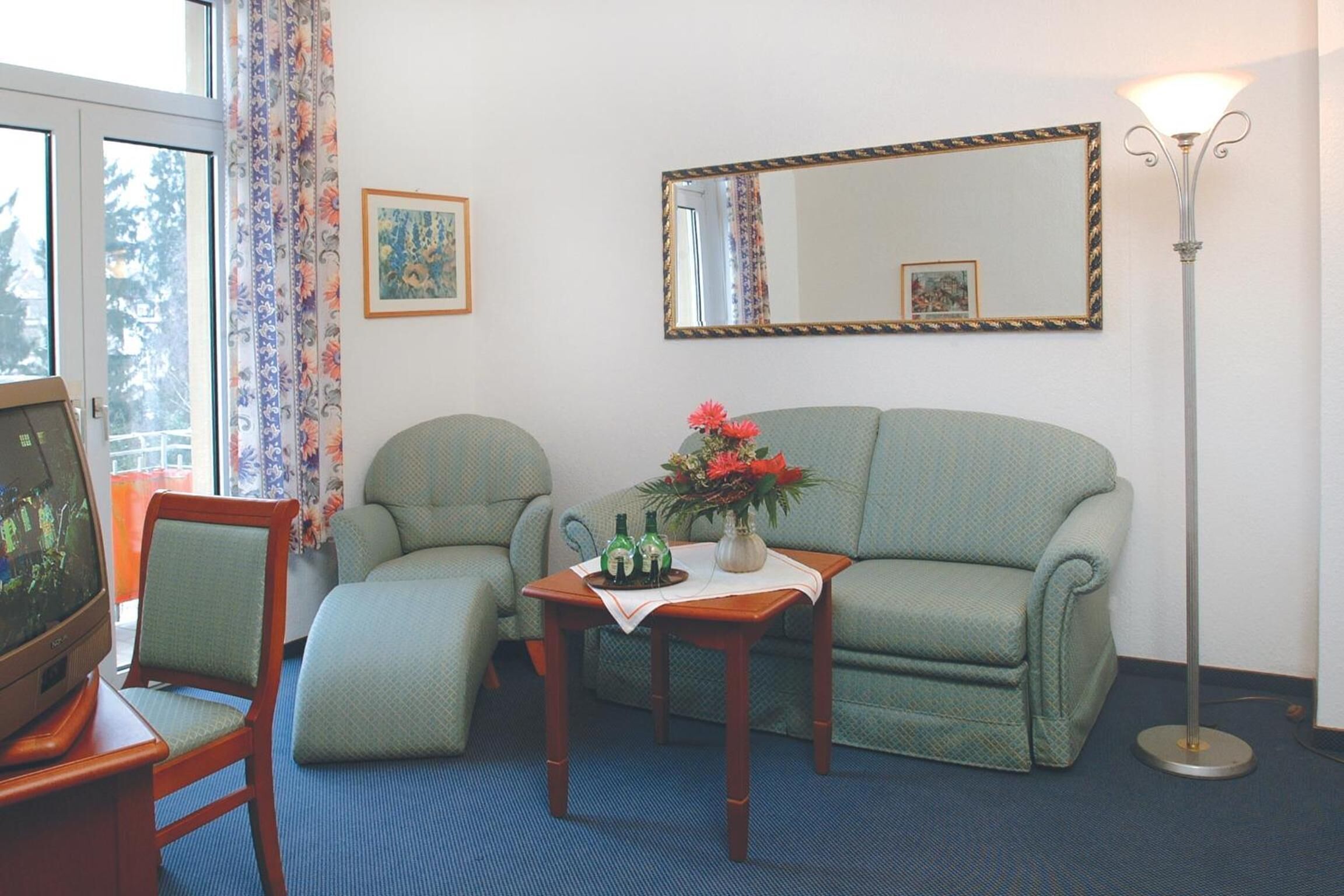 Uma sala de estar com sofá, duas poltronas, uma mesa de centro com um vaso de flores, televisão e abajur.