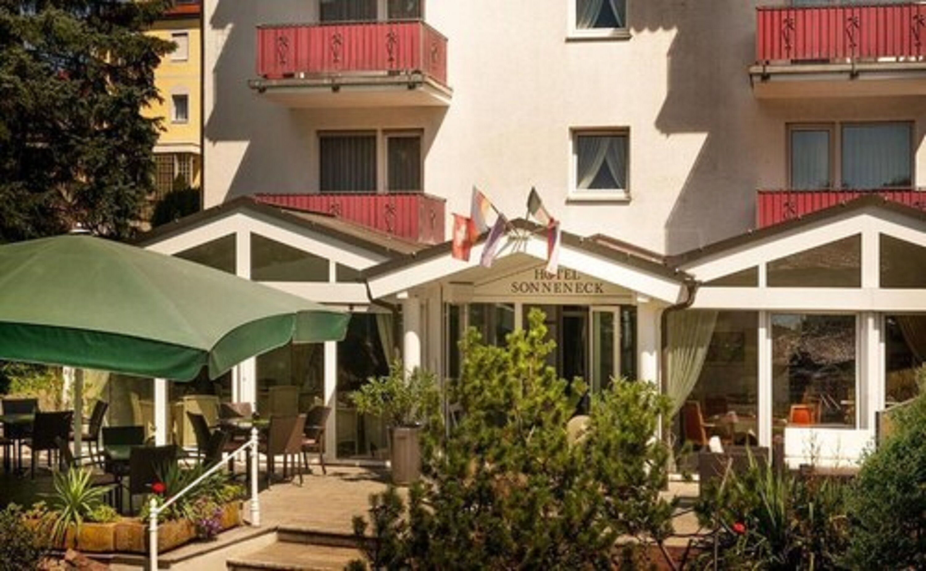 Een hotel met een overdekte buitenruimte, een bord met daarop 'Hotel Sonnenheck' en een rode balkonbalustrade.
