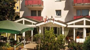 Een hotel met een overdekte buitenruimte, een bord met daarop 'Hotel Sonnenheck' en een rode balkonbalustrade.