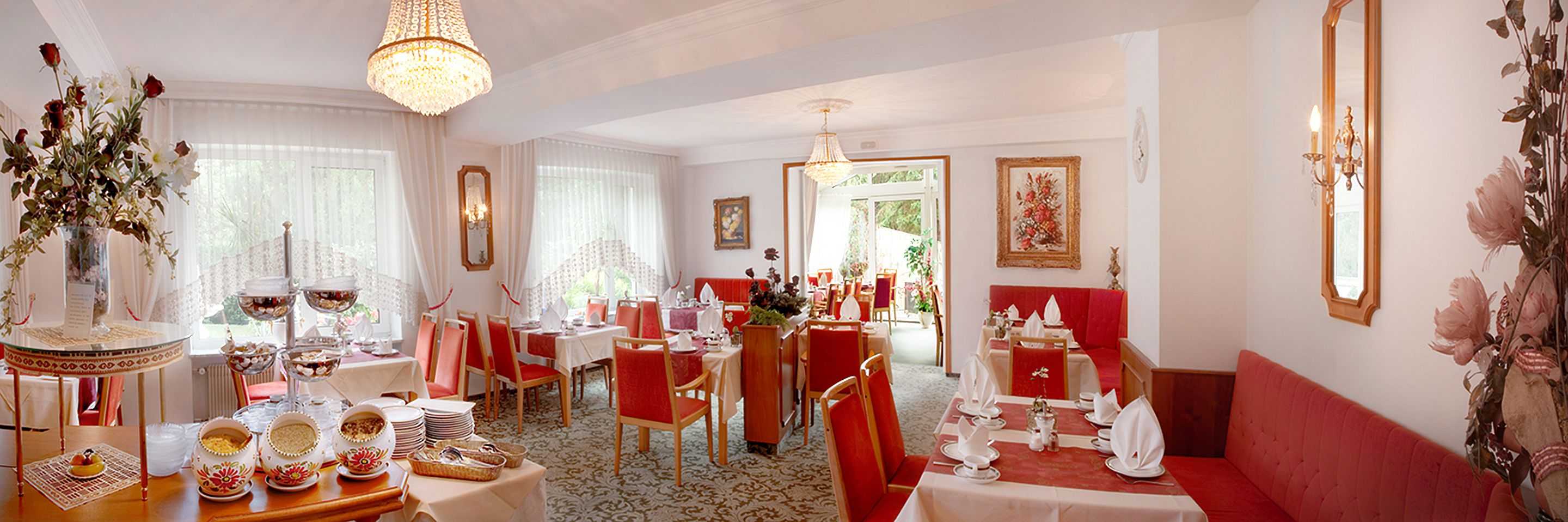 A dining area with tables set for service, a chandelier, and a red sofa.