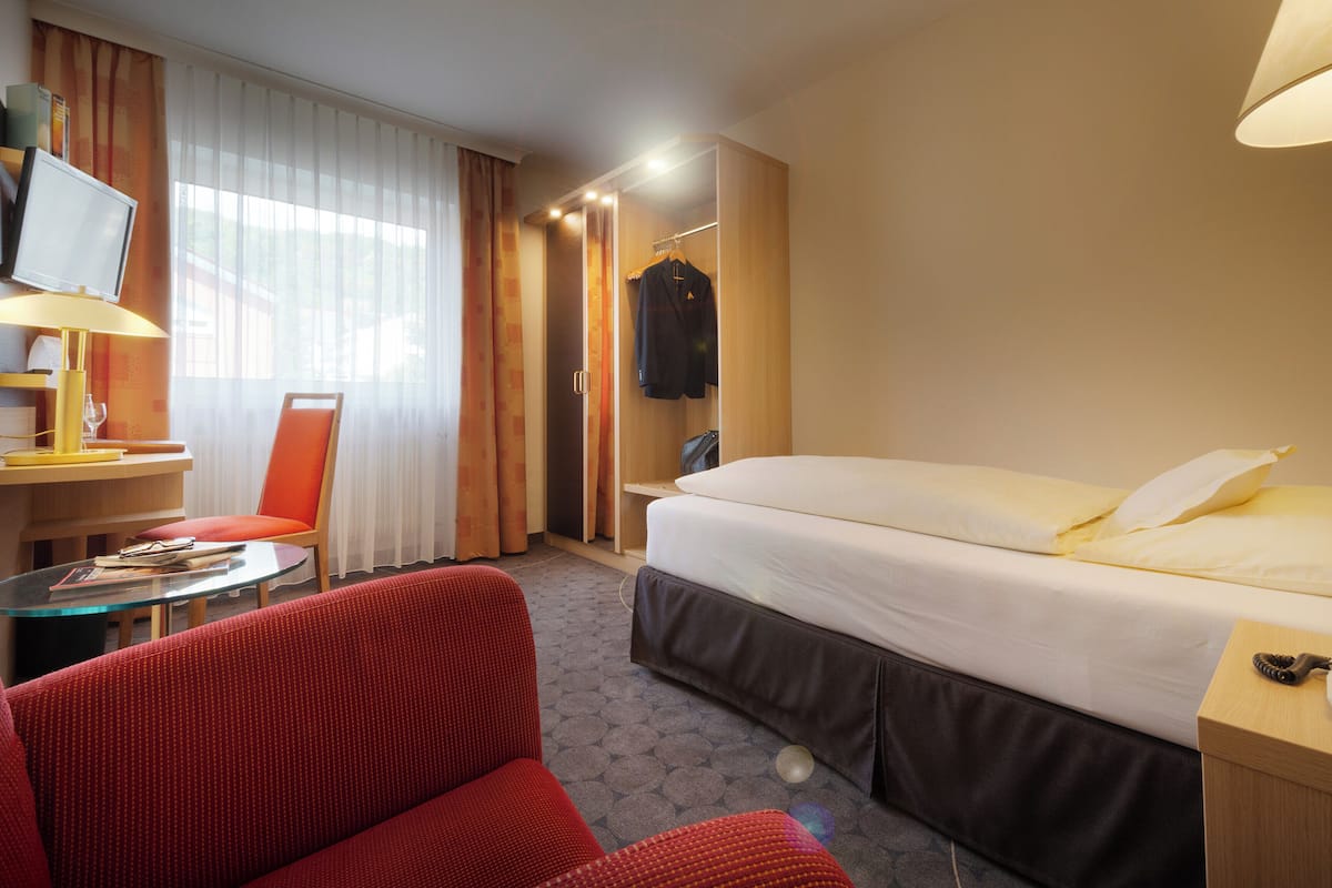 A hotel room with a bed, a desk with a computer, a chair, and a telephone.