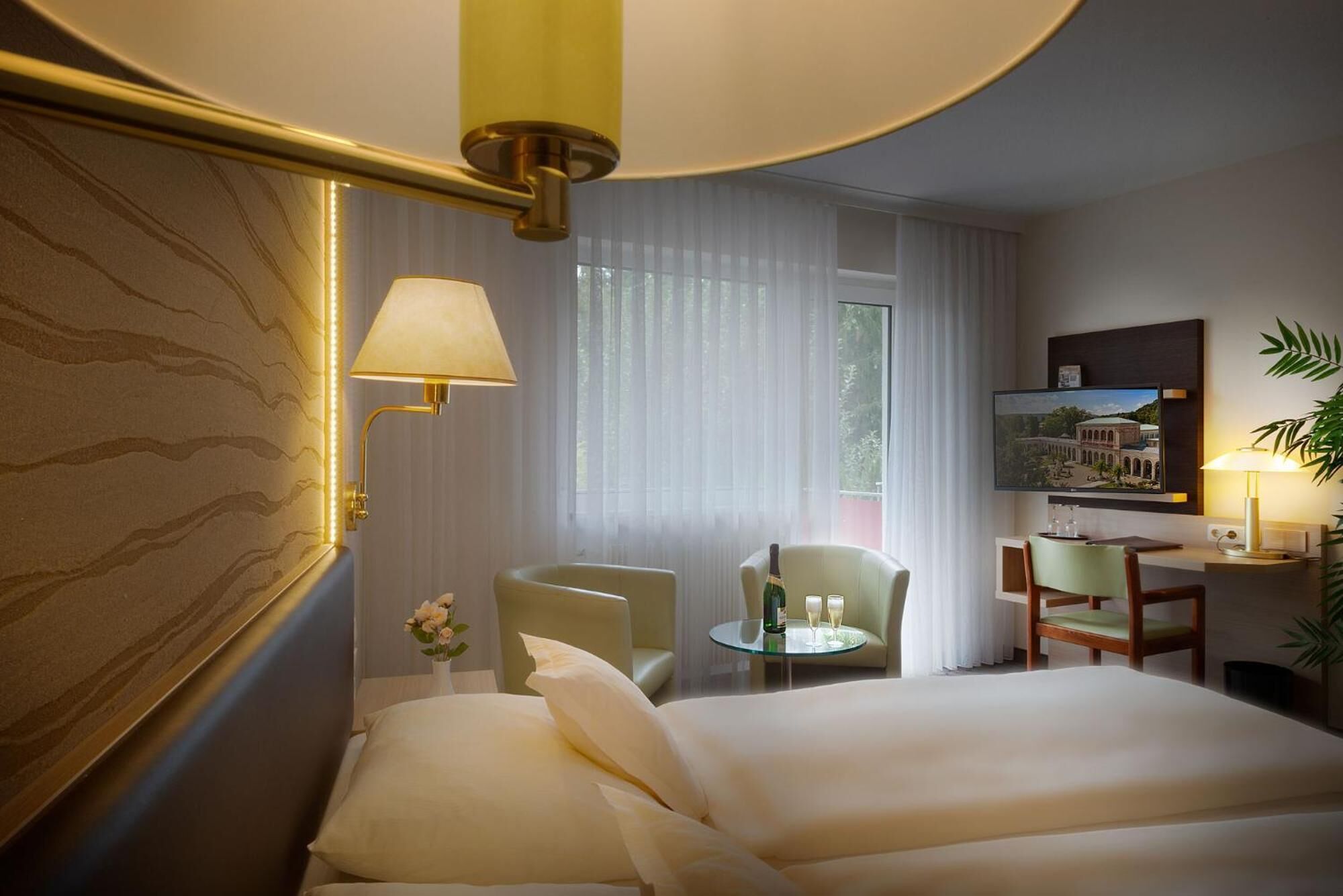 A hotel room with two beds, a desk, a chair, a TV, and a window with curtains.