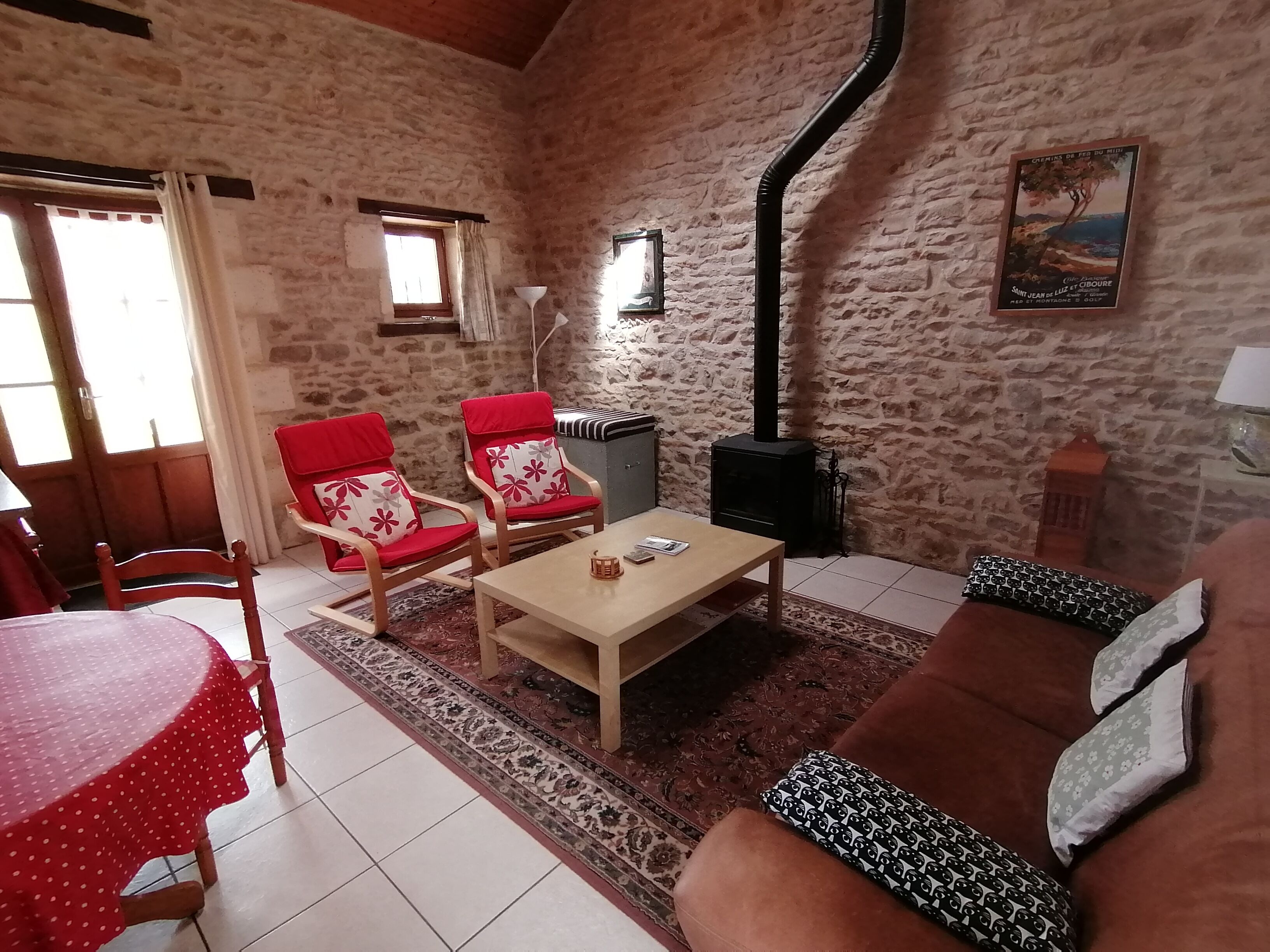 Una sala de estar acogedora con pared de piedra, una mesa de madera, dos sillas rojas, un sofá marrón y una chimenea.