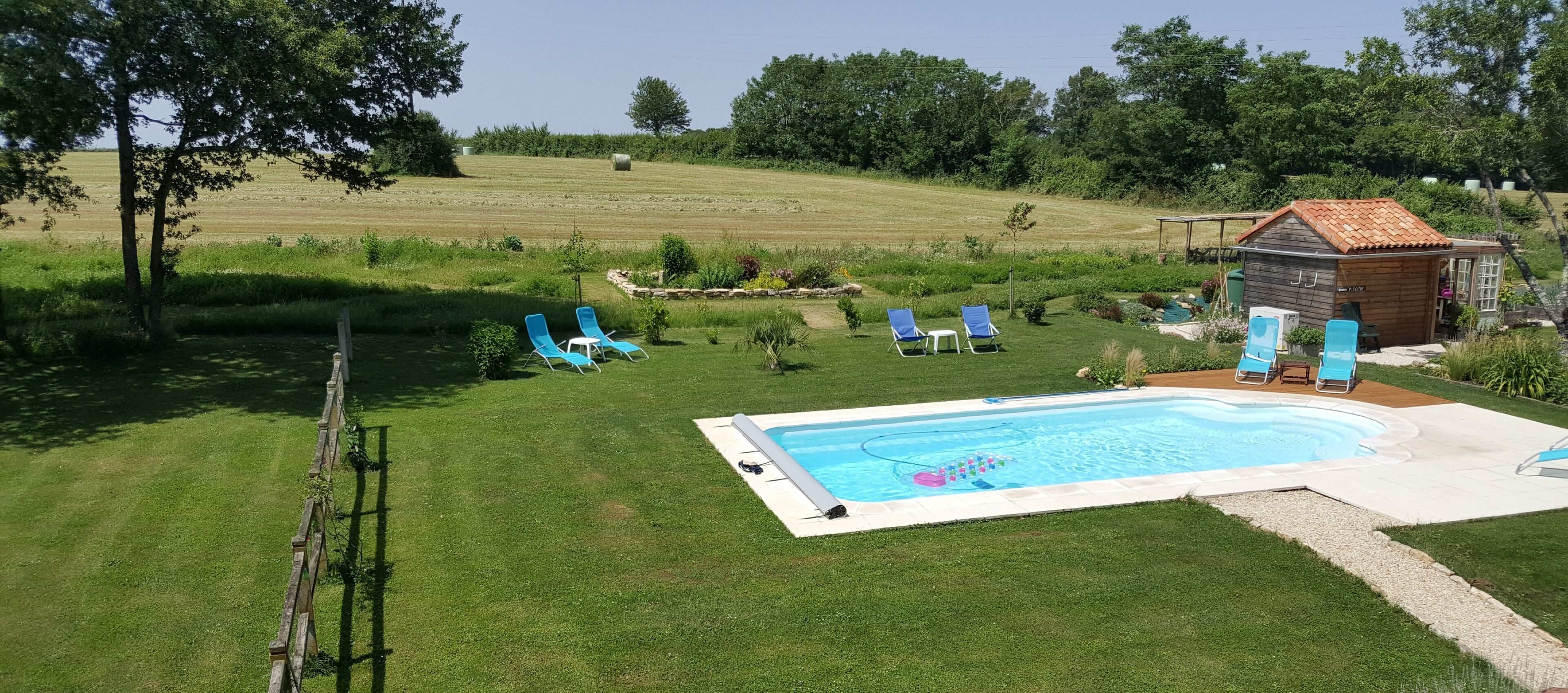 A swimming pool with blue lounge chairs, a wooden shed, and a grassy field in the background.