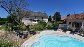Een zwembad met ligbedden, omgeven door een tuin met verschillende planten en een huis op de achtergrond.