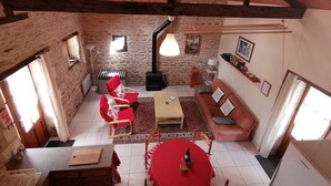 Een gezellige kamer met een stenen muur, houten balken, een rode bank, een houten tafel en een rood tafelkleed.