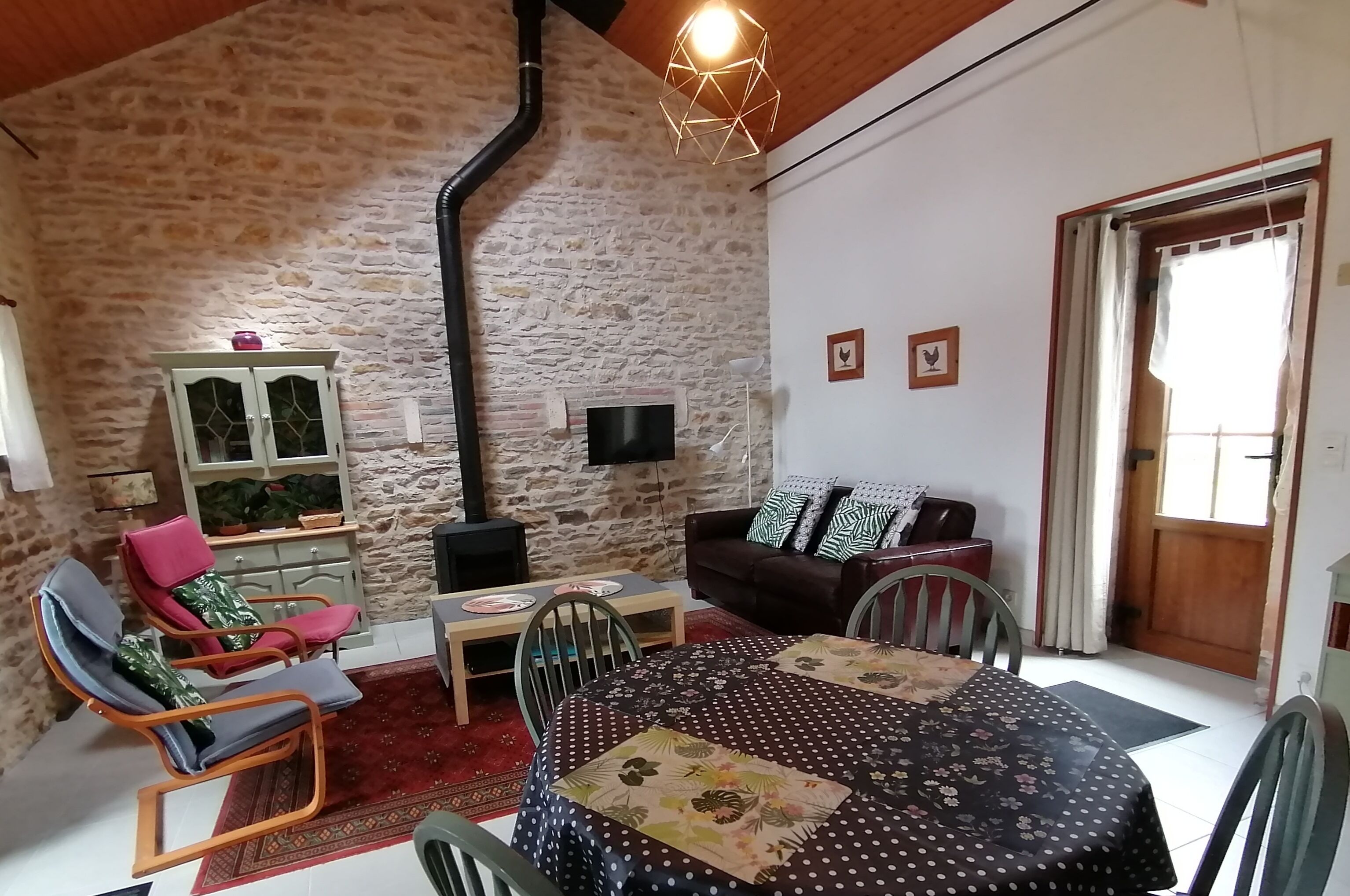 Una sala de estar acogedora con pared de piedra, techo de madera, mesa de comedor con sillas, un sofá y un televisor.
