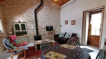 Una sala de estar acogedora con pared de piedra, techo de madera, mesa de comedor con sillas, un sofá y un televisor.