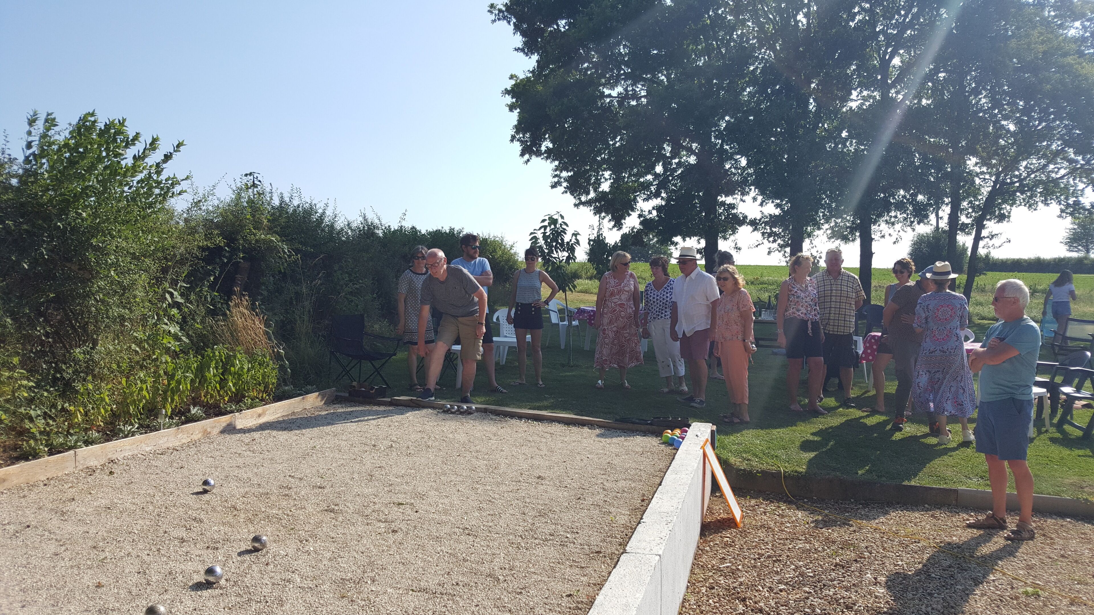 A group of people gathered around a croquet field with a wooden fence and a small table with a cloth.