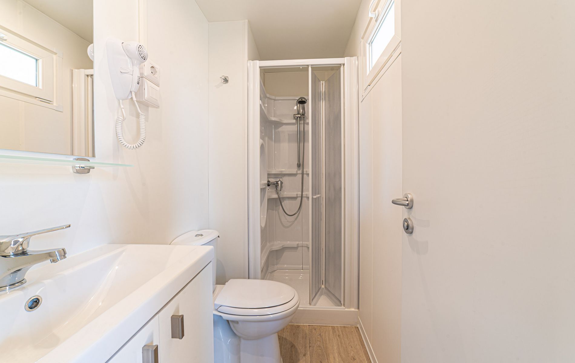 A compact bathroom with a toilet, a glass shower enclosure, and a white sink.
