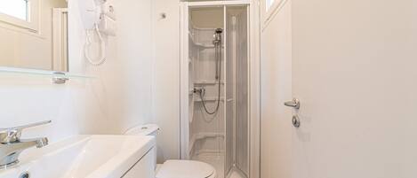 A compact bathroom with a toilet, a glass shower enclosure, and a white sink.