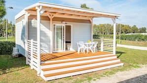 A small, single-story building with a covered porch, a sliding glass door, and a small outdoor seating area with white chairs and a table. - Camping Village Roma Capitol (Rome)