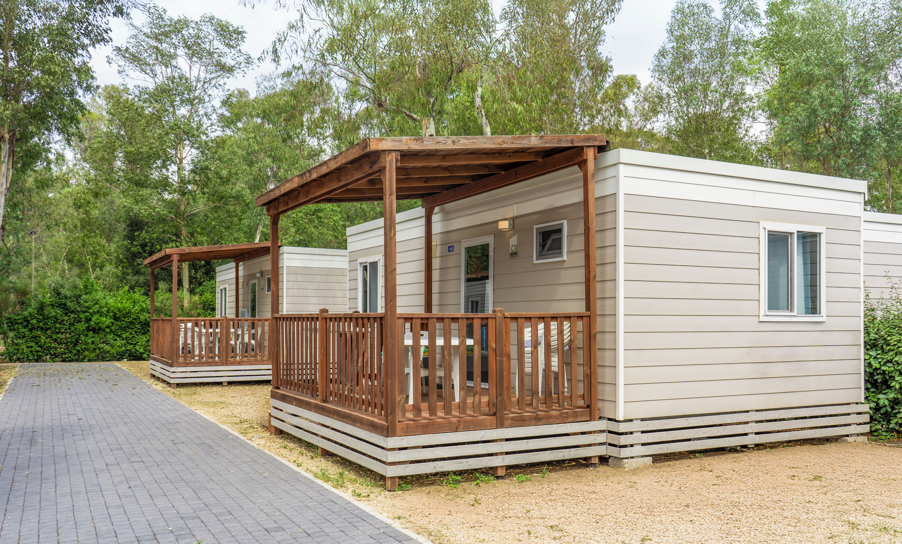 Una hilera de casas móviles con terrazas y barandillas de madera, rodeadas de árboles.