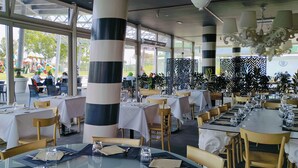 A restaurant with outdoor seating, large windows, and a view of a playground. Tables are set with white tablecloths and chairs. - Camping Village Roma Capitol (Rome)