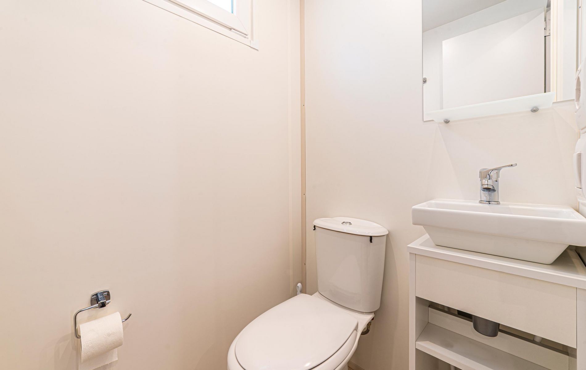 A small, clean bathroom with a toilet, sink, and mirror.