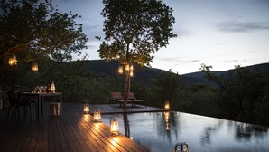 En træterrasse med pool, omgivet af træer og et bjergrigt baggrundsmotiv.