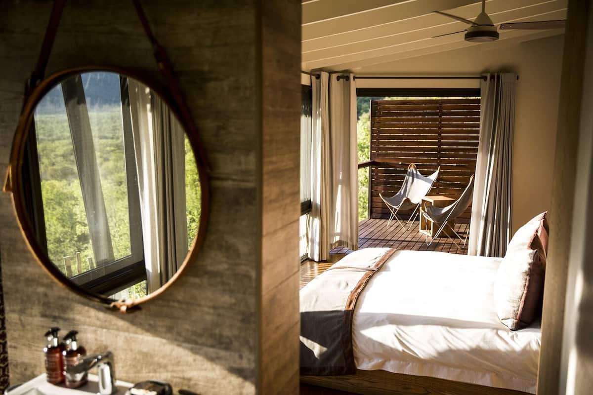 Ein Schlafzimmer mit Bett, Fenster, Spiegel und Blick ins Freie.