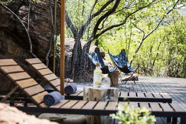 A wooden deck with lounge chairs, a hammock, and a water feature.