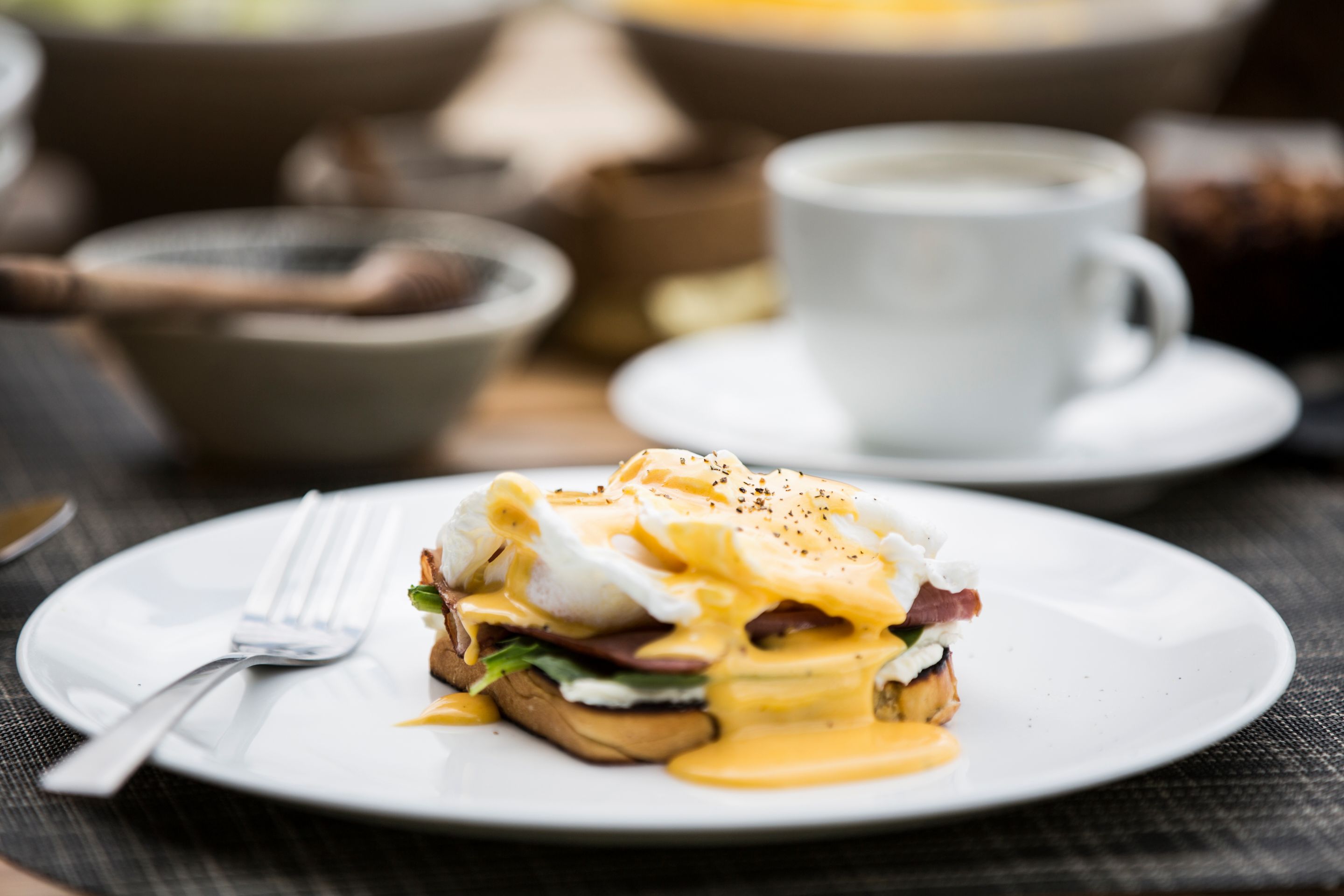 Une assiette de petit-déjeuner avec des œufs Bénédicte, une fourchette et une tasse de café, le tout posé sur une table.