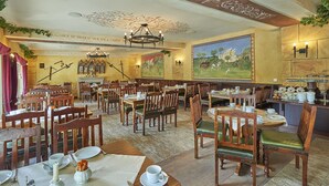 A dining area with wooden tables and chairs, a chandelier, and a mural on the wall. - Hotel Elbparadies (Pirna)