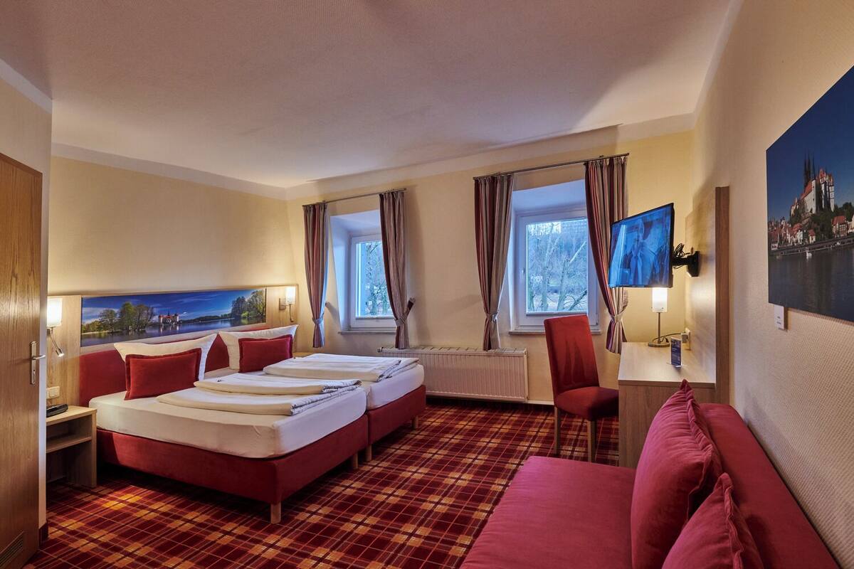 A hotel room with a bed, two bedside tables, a desk, a chair, and a TV.