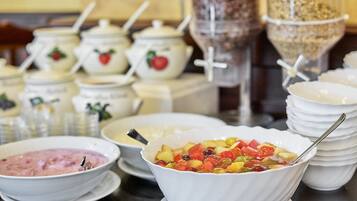 En buffet med forskellige retter, herunder en skål frugtsalat, en skål suppe og flere beholdere med tilbehør.