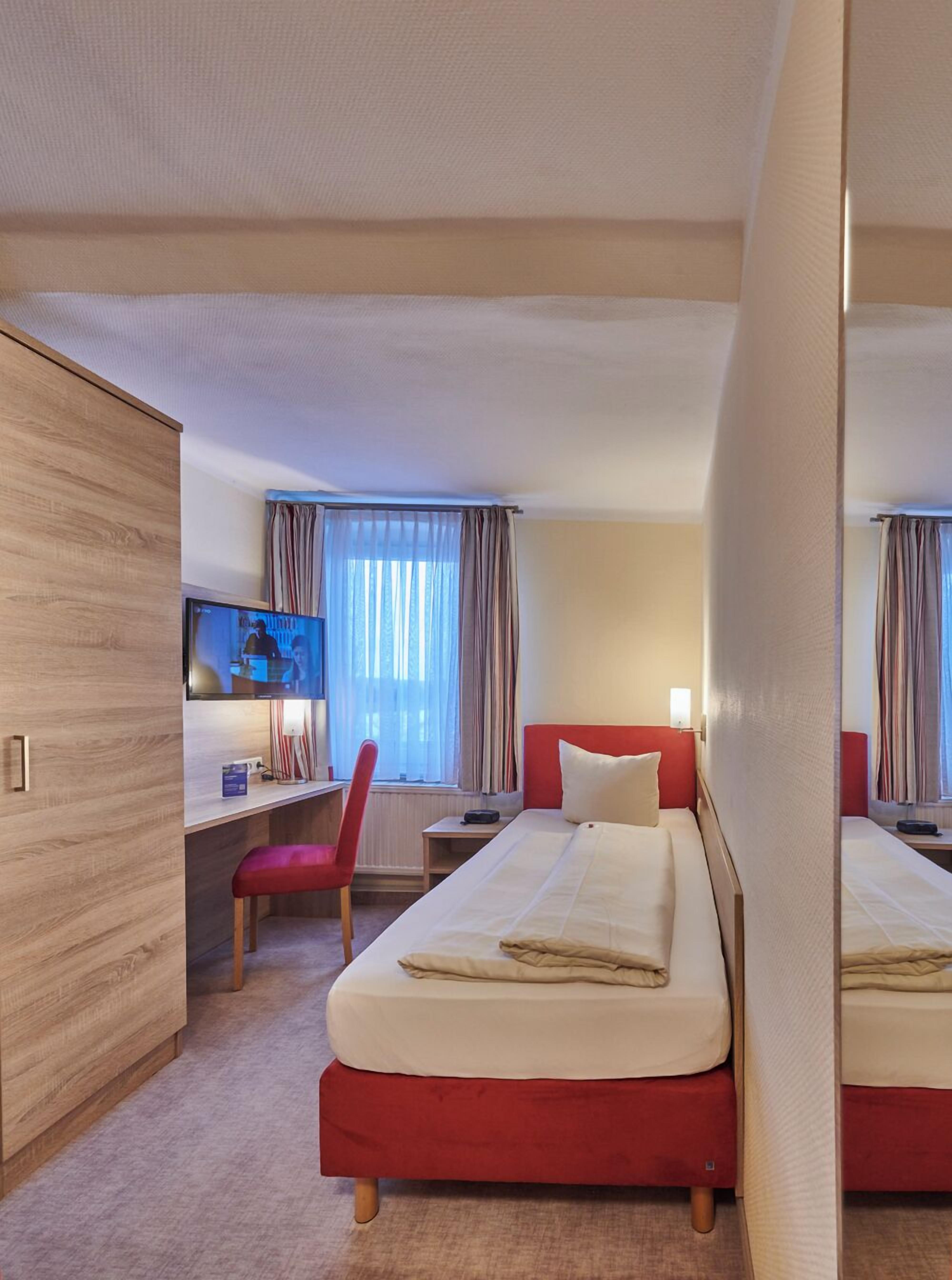 A hotel room with two beds, a desk, a chair, and a television.